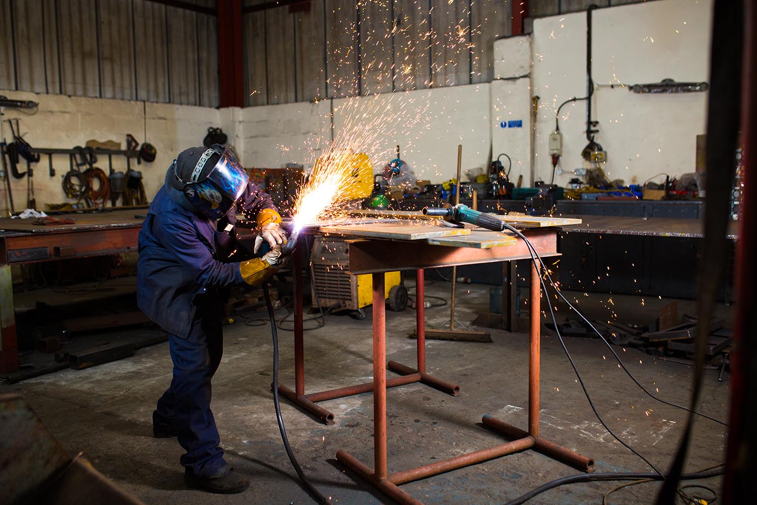 Engineer in welding mask grinding steel with sparks flying